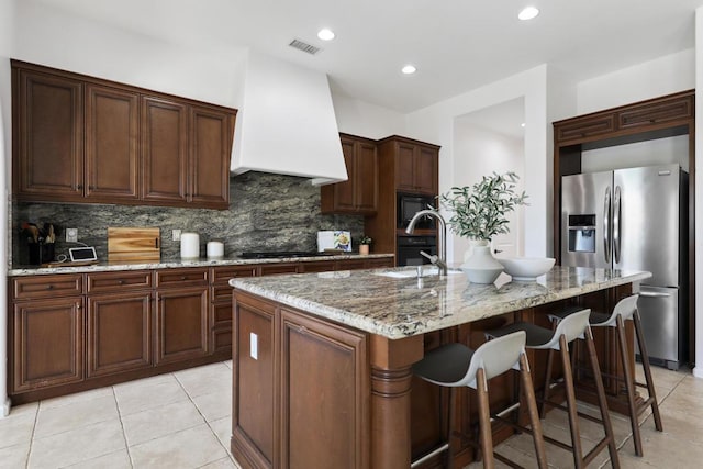 kitchen featuring sink, tasteful backsplash, a center island with sink, black appliances, and custom range hood