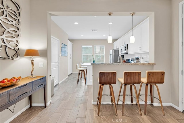 kitchen with pendant lighting, appliances with stainless steel finishes, white cabinets, a kitchen bar, and kitchen peninsula