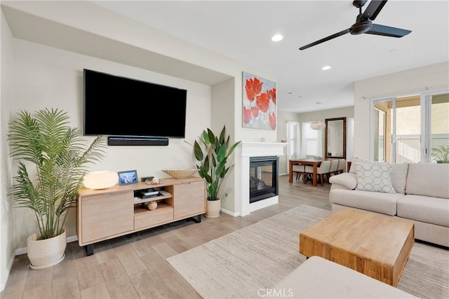 living room with recessed lighting, light wood-style floors, a multi sided fireplace, ceiling fan, and baseboards