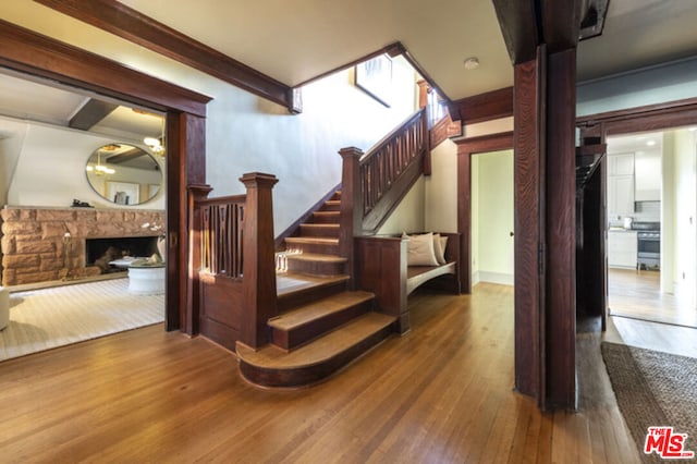 staircase with hardwood / wood-style floors, beam ceiling, and a stone fireplace