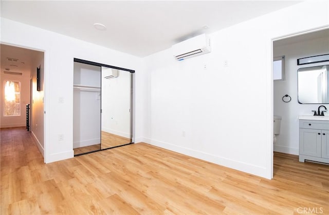 unfurnished bedroom with ensuite bath, sink, light hardwood / wood-style flooring, an AC wall unit, and a closet