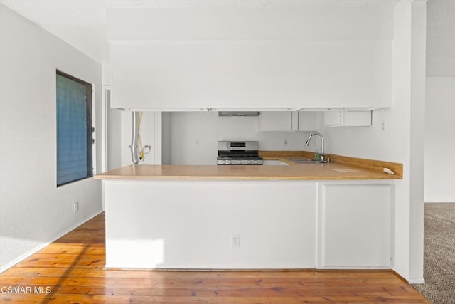 kitchen featuring hardwood / wood-style floors, gas stove, kitchen peninsula, and sink