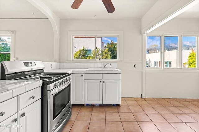 kitchen featuring sink, stainless steel gas range, tile countertops, and white cabinetry