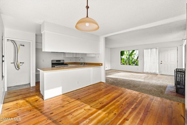 kitchen featuring light colored carpet, pendant lighting, kitchen peninsula, sink, and stainless steel gas range