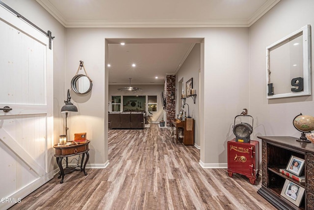 hall with a barn door, wood-type flooring, and ornamental molding