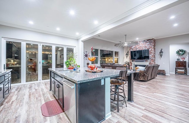 kitchen with stainless steel dishwasher, a fireplace, a center island with sink, and light wood-type flooring