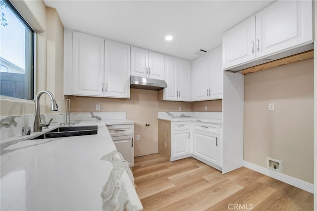 kitchen with light stone countertops, light hardwood / wood-style floors, white cabinetry, and sink