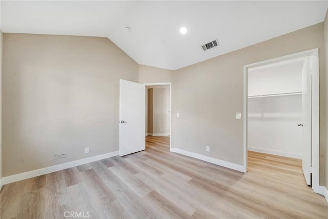 unfurnished bedroom with a closet, light hardwood / wood-style floors, vaulted ceiling, and a spacious closet