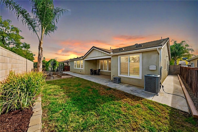 back house at dusk with a lawn, a patio, and central AC unit