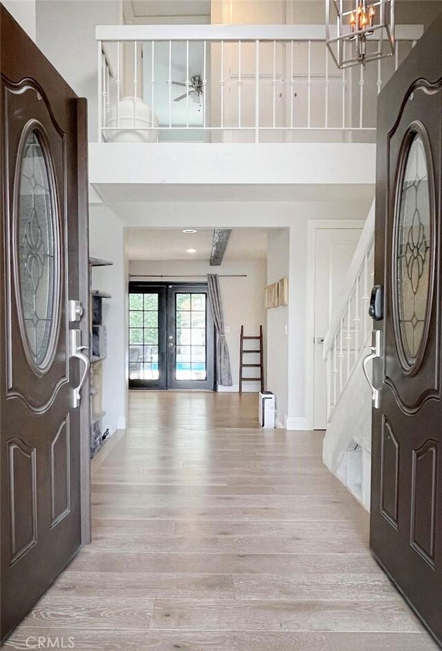 foyer entrance featuring french doors, a towering ceiling, light hardwood / wood-style floors, and a notable chandelier