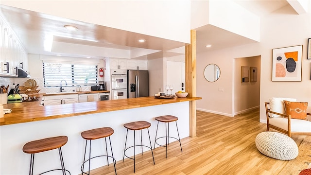 kitchen featuring kitchen peninsula, sink, white cabinets, stainless steel fridge with ice dispenser, and a breakfast bar area