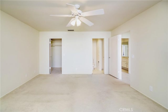 unfurnished bedroom featuring a closet, ensuite bathroom, light colored carpet, and ceiling fan