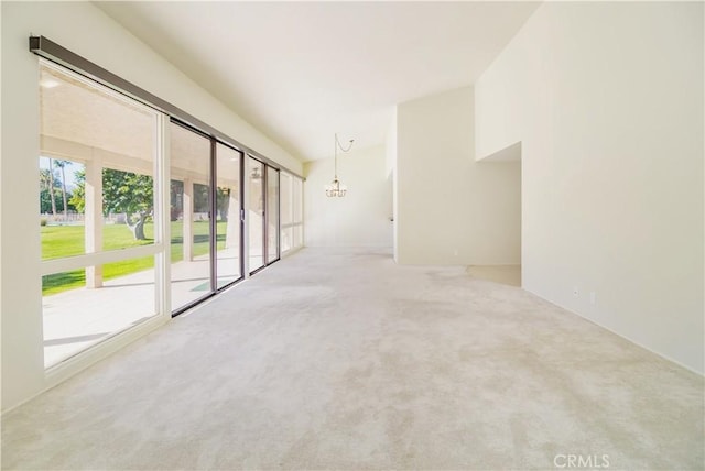 carpeted spare room with vaulted ceiling and an inviting chandelier