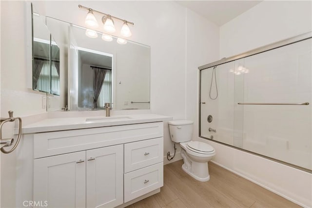 full bathroom with vanity, hardwood / wood-style flooring, toilet, and bath / shower combo with glass door