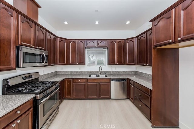 kitchen with appliances with stainless steel finishes, light wood-type flooring, light stone counters, and sink