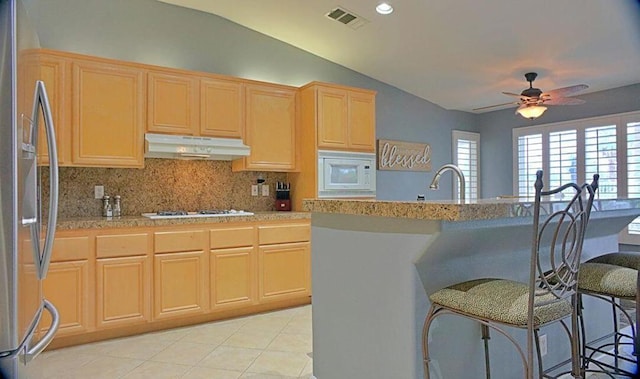 kitchen with a breakfast bar, light brown cabinets, white appliances, and lofted ceiling