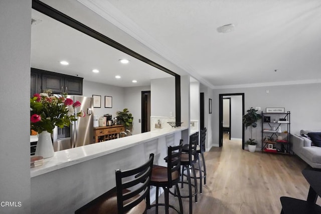 kitchen with kitchen peninsula, stainless steel fridge, light wood-type flooring, a kitchen bar, and crown molding