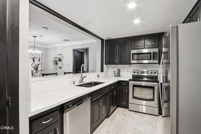 kitchen with sink, stainless steel appliances, an inviting chandelier, light hardwood / wood-style flooring, and ornamental molding