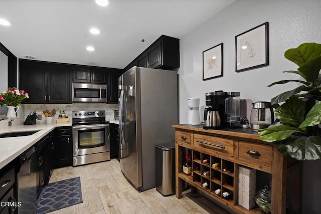 kitchen with appliances with stainless steel finishes, backsplash, light hardwood / wood-style floors, and sink