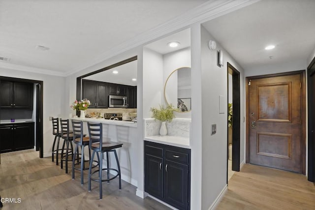 kitchen with stainless steel appliances, tasteful backsplash, light hardwood / wood-style flooring, crown molding, and a kitchen bar