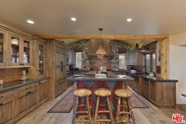 kitchen featuring pendant lighting, light wood-type flooring, a kitchen island, and custom range hood