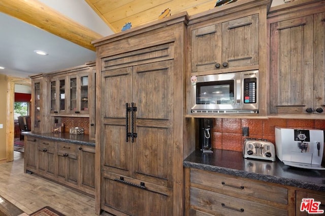 kitchen with light hardwood / wood-style floors, stainless steel microwave, lofted ceiling, and dark stone counters