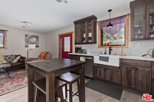 kitchen featuring dark brown cabinetry, dishwasher, sink, hanging light fixtures, and light wood-type flooring