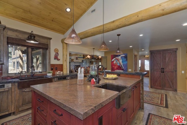 kitchen featuring vaulted ceiling, a kitchen island with sink, sink, light hardwood / wood-style floors, and hanging light fixtures