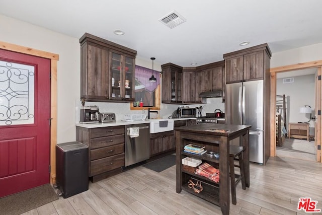 kitchen featuring appliances with stainless steel finishes, dark brown cabinetry, sink, decorative light fixtures, and light hardwood / wood-style flooring