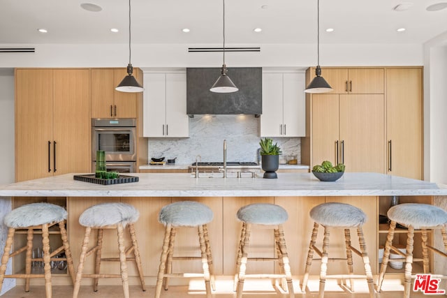 kitchen featuring a kitchen island with sink, pendant lighting, white cabinets, and light brown cabinets