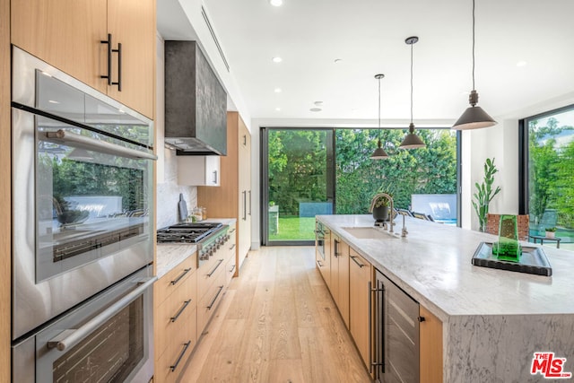 kitchen featuring sink, stainless steel appliances, decorative light fixtures, a large island with sink, and light brown cabinets