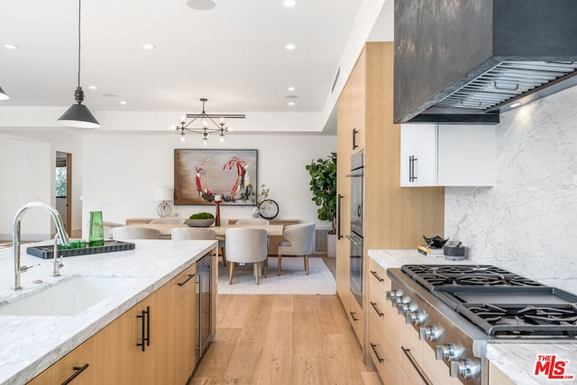 kitchen featuring stainless steel gas stovetop, sink, hanging light fixtures, light stone countertops, and custom range hood