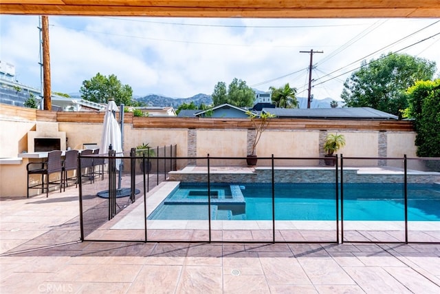 view of swimming pool featuring a mountain view, a patio, exterior fireplace, and a hot tub