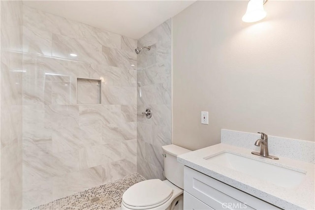 bathroom featuring a tile shower, vanity, and toilet