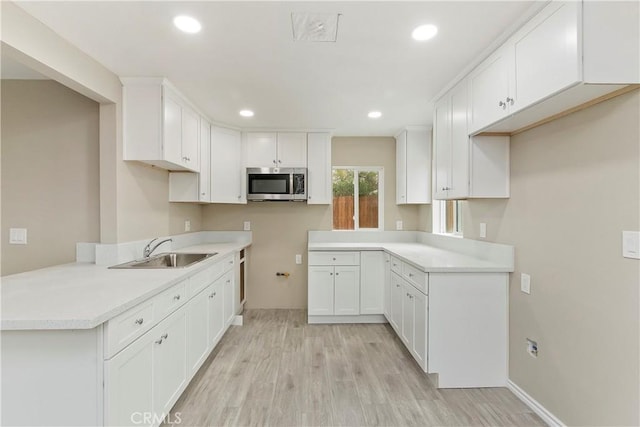 kitchen featuring kitchen peninsula, white cabinetry, sink, and light hardwood / wood-style flooring