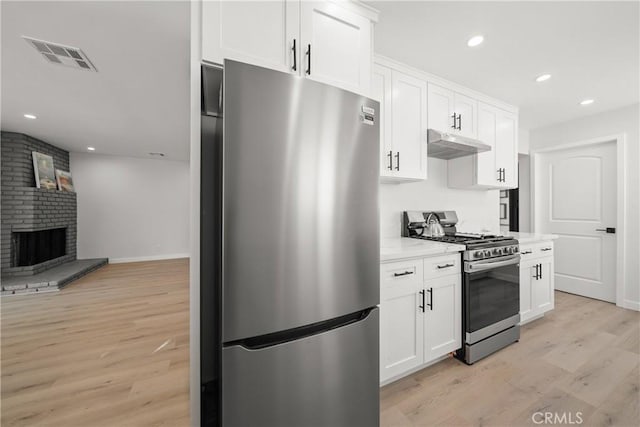 kitchen with appliances with stainless steel finishes, white cabinetry, a fireplace, light wood-type flooring, and light stone counters