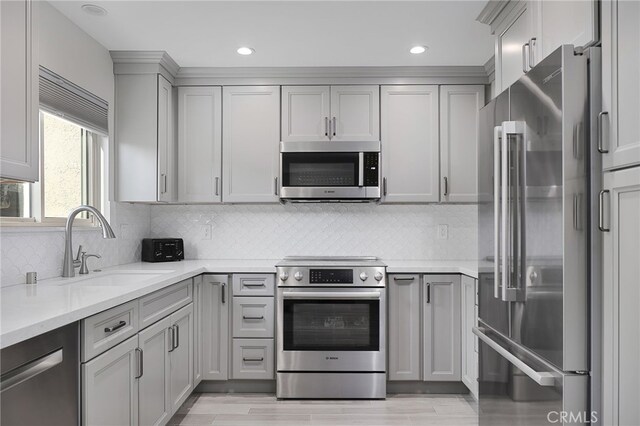 kitchen with appliances with stainless steel finishes, sink, backsplash, gray cabinets, and light stone counters