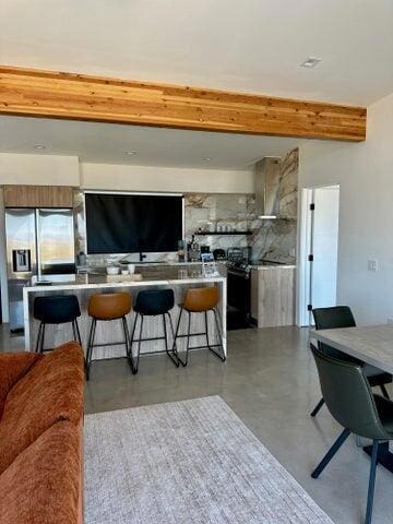 kitchen featuring beam ceiling, a breakfast bar, and stainless steel refrigerator with ice dispenser