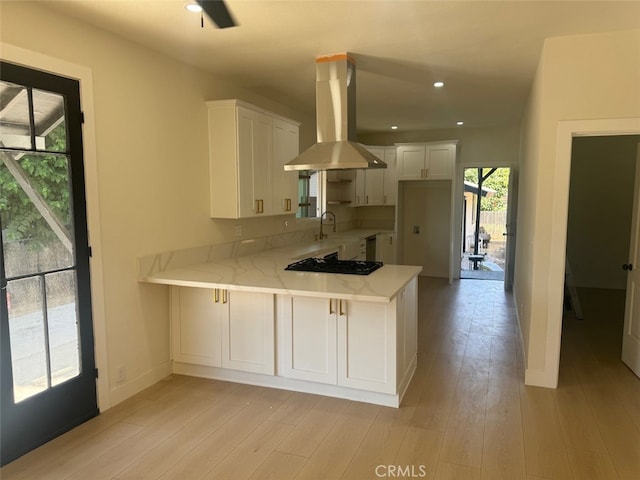 kitchen featuring light stone countertops, black gas stovetop, white cabinetry, kitchen peninsula, and island range hood