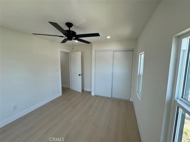 unfurnished bedroom with ceiling fan, a closet, light wood-type flooring, and multiple windows