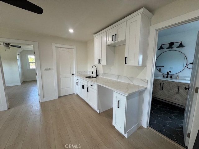 kitchen featuring ceiling fan, white cabinets, sink, and light stone counters