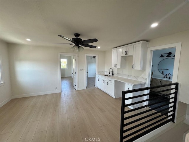 kitchen featuring white cabinets, light wood-type flooring, light stone countertops, and sink