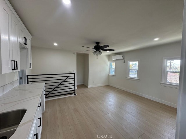 interior space with an AC wall unit, sink, ceiling fan, and light hardwood / wood-style floors