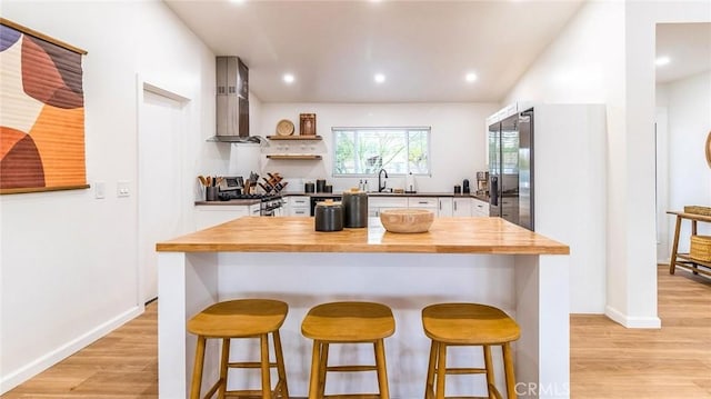 kitchen featuring stainless steel range with gas cooktop, sink, wall chimney range hood, light hardwood / wood-style floors, and white cabinetry