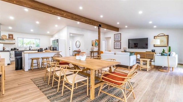 dining space featuring lofted ceiling with beams, sink, and light hardwood / wood-style flooring