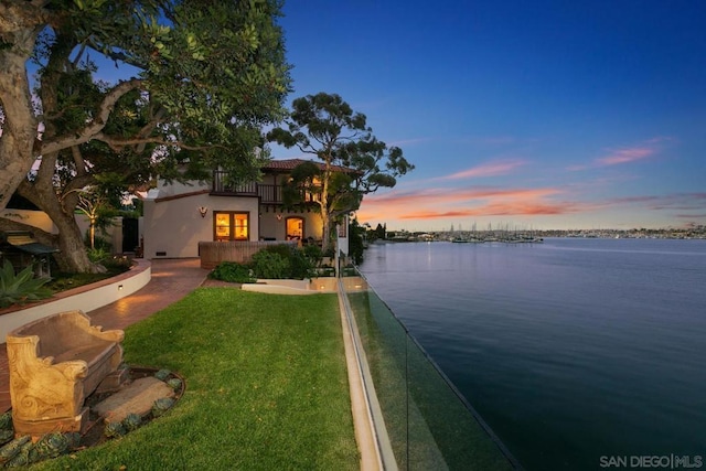 view of front of house featuring a water view, a balcony, and a lawn