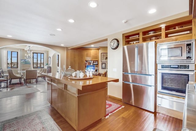 kitchen with a chandelier, a kitchen island, light wood-type flooring, and appliances with stainless steel finishes