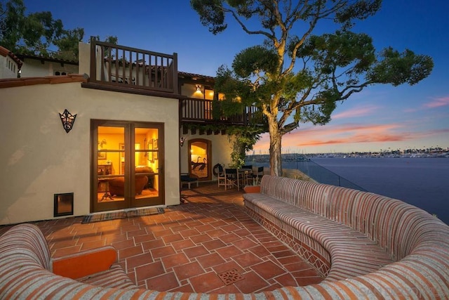 patio terrace at dusk featuring an outdoor living space, a balcony, a water view, and french doors