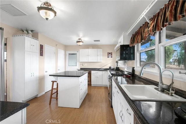 kitchen with stainless steel range, a center island, white cabinets, and sink