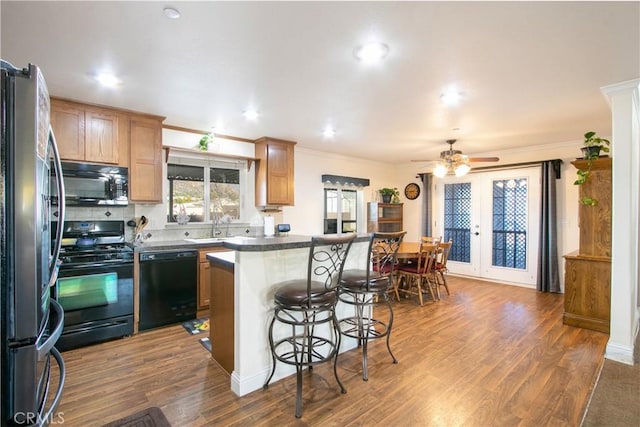 kitchen with french doors, wood-type flooring, a breakfast bar area, a kitchen island, and black appliances